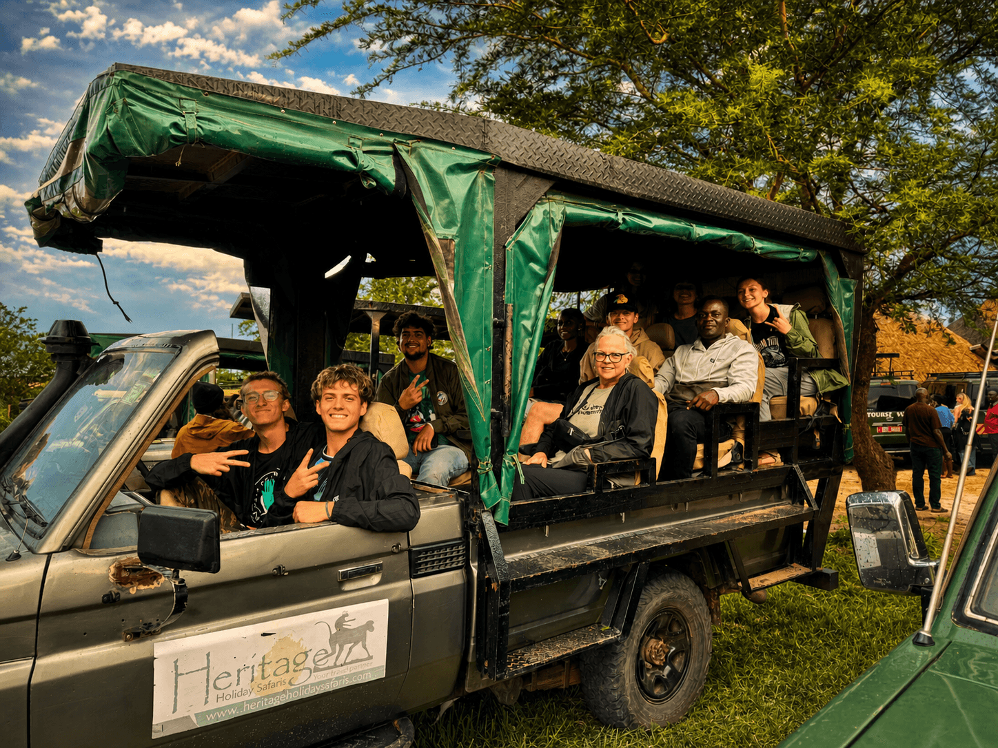 A group of guests smiling in a green open-sided safari vehicle at The Elephant Oasis, ready for a game drive