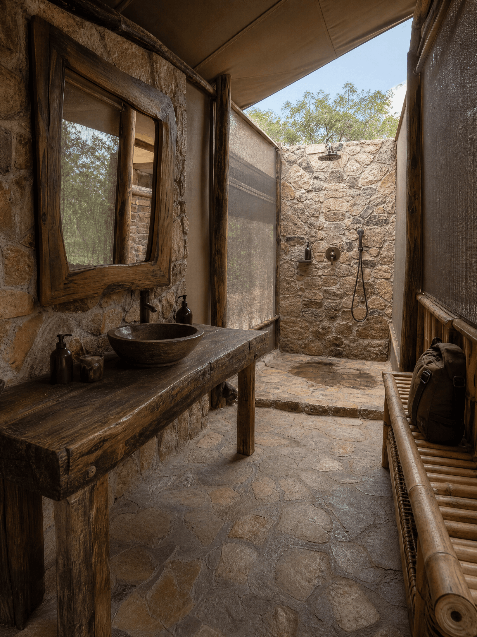 Luxury Safari Tent en suite bathroom at The Elephant Oasis — natural stone floor and walls, rough-hewn African hardwood vanity, stone basin, overhead shower open to the sky, bamboo and wood luggage rack, Murchison Falls Uganda
