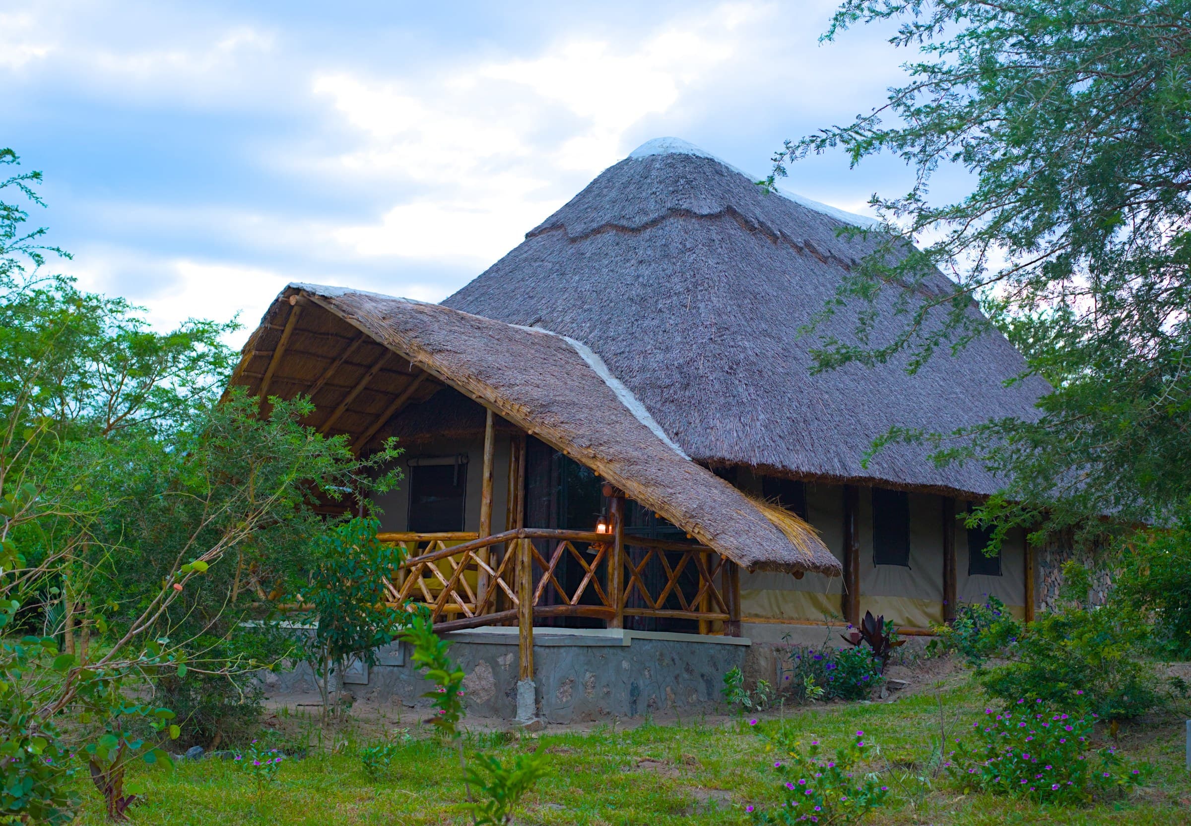 Safari tent exterior at The Elephant Oasis with thatched roof, timber deck, and garden, Murchison Falls Uganda